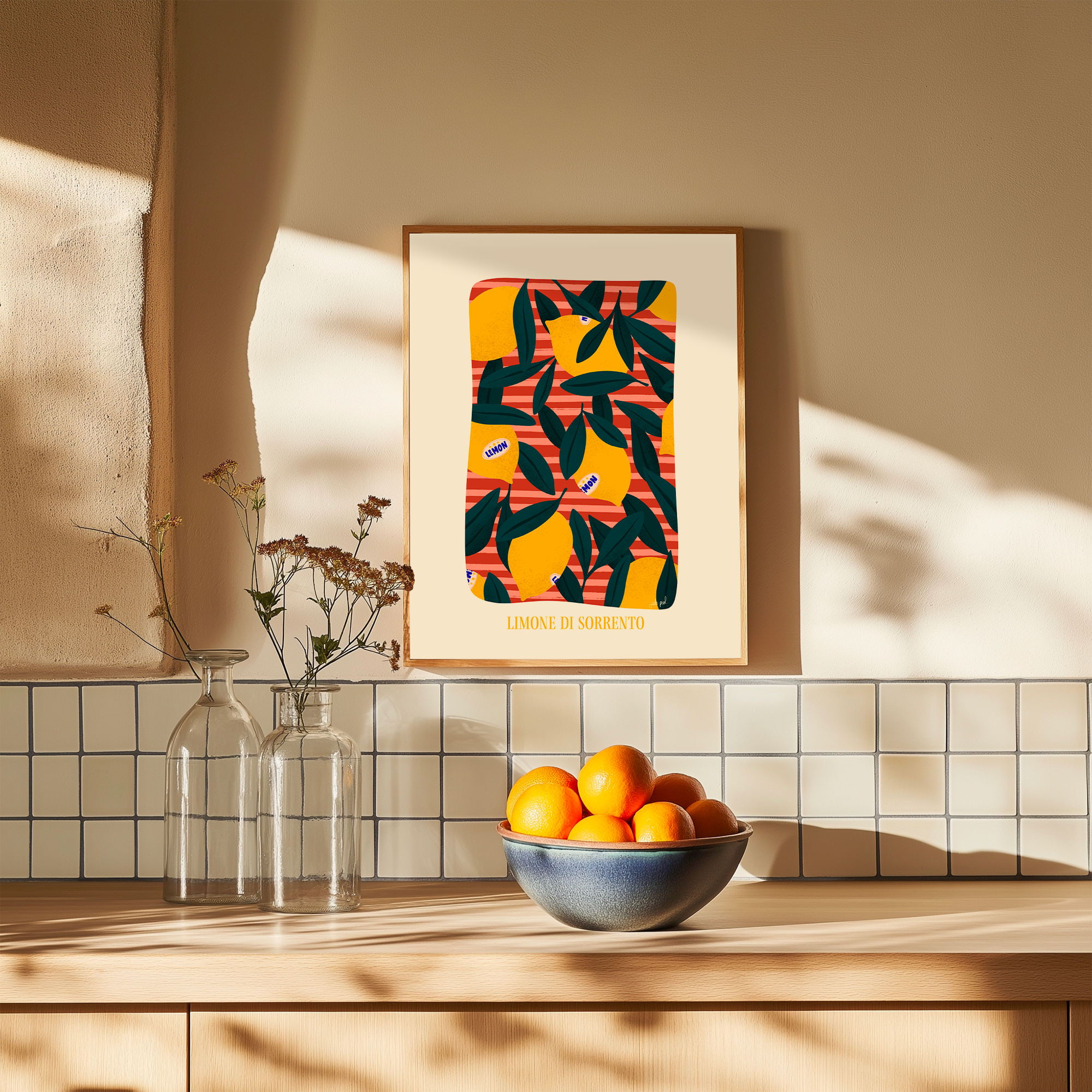 Affiche illustrée de citrons jaunes et feuillage vert encadrée, accrochée au-dessus d’un plan de travail avec bol d’agrumes et vases en verre dans une cuisine lumineuse.