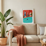 Affiche illustrée colorée représentant une piscine intérieure encadrée et posée au-dessus d’un canapé beige, dans un salon lumineux avec plante verte et coussins.