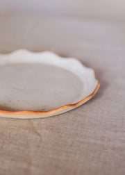 Une assiette en grès avec des bords ondulés de couleur gris clair.