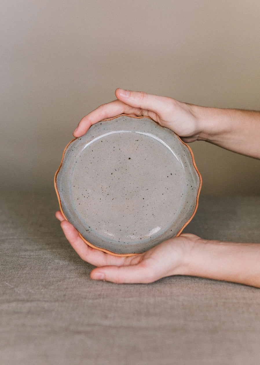 Une assiette en grès avec des bords ondulés de couleur gris clair tenue par une personne.