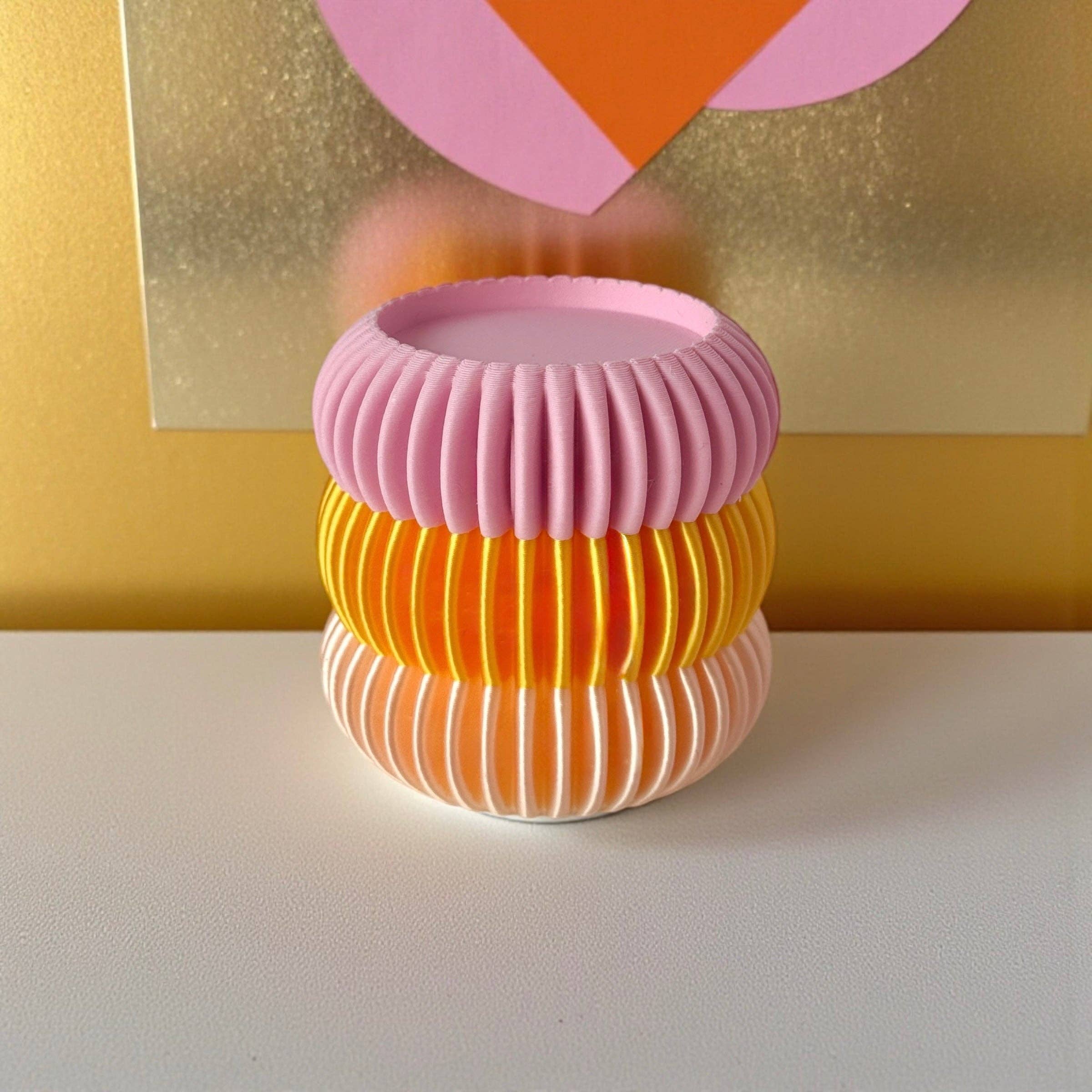 Bougeoir design nervuré aux tons rose, orange et blanc, posé sur une table blanche dans un univers déco pop et lumineux.