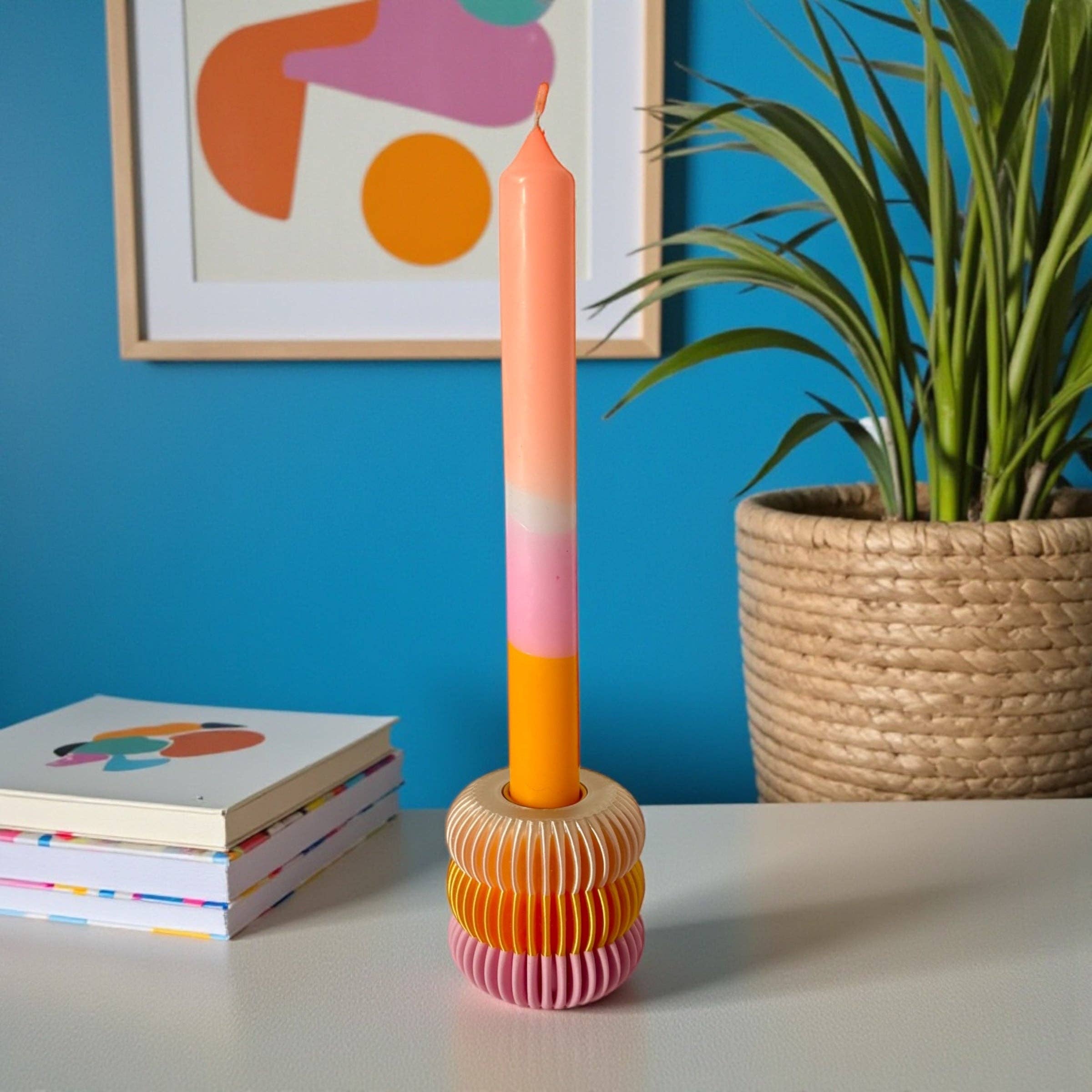 Bougeoir design nervuré aux tons rose, orange et blanc, posé sur une table blanche dans un univers déco pop et lumineux.
