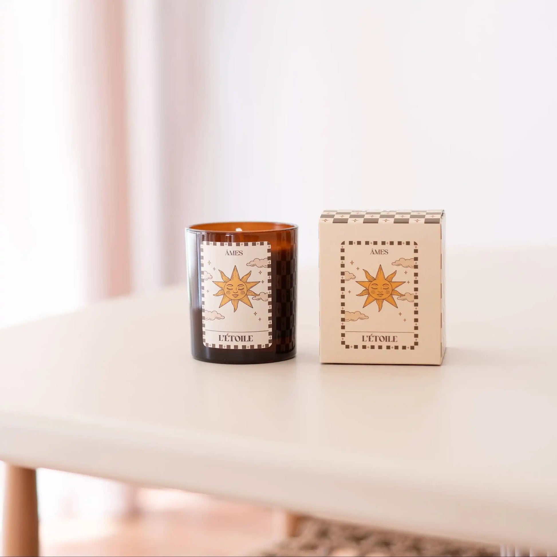 Une bougie parfumée AMES “L’Étoile” accompagnée de son coffret assorti, posés sur une table claire dans une ambiance douce et lumineuse.