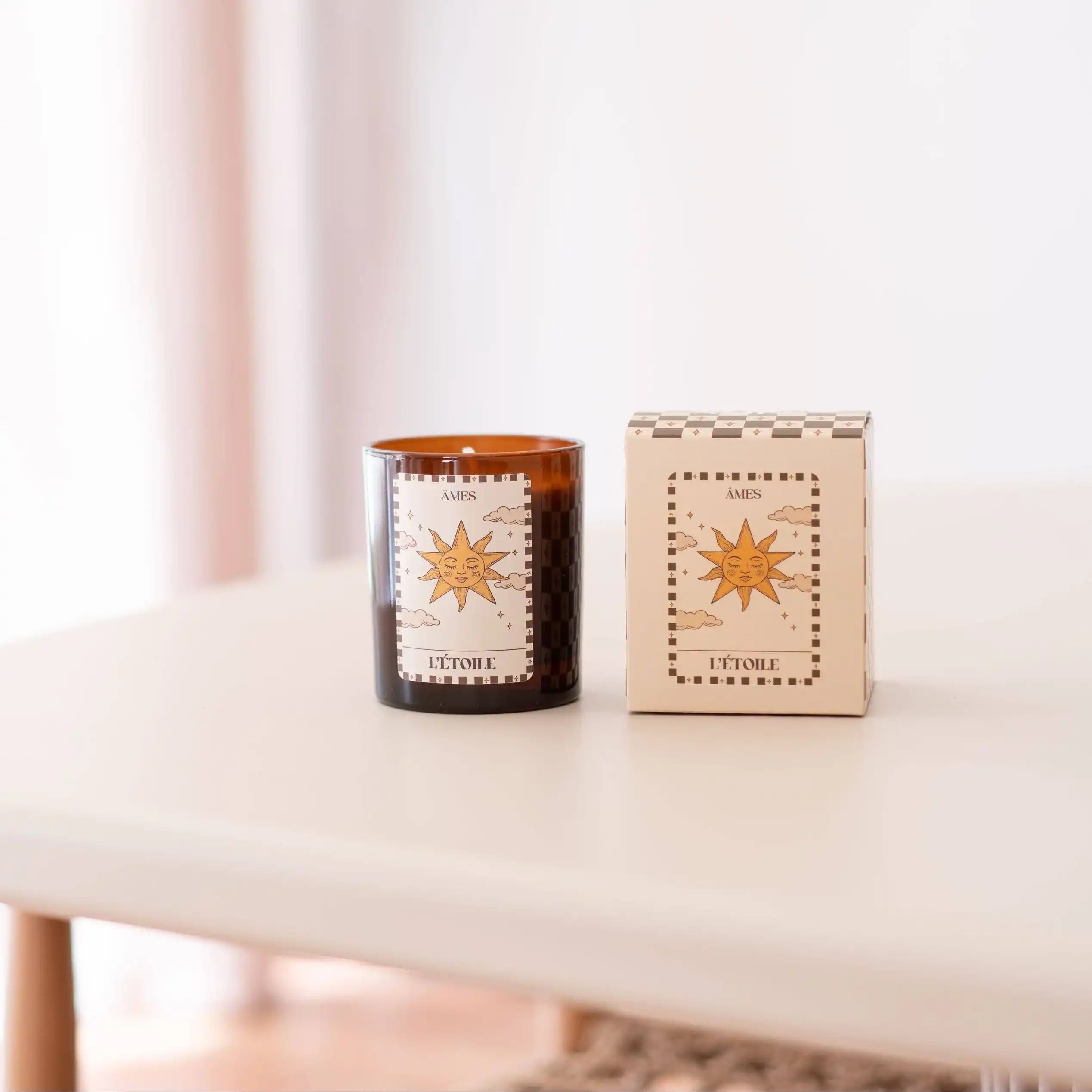 Une bougie parfumée AMES “L’Étoile” accompagnée de son coffret assorti, posés sur une table claire dans une ambiance douce et lumineuse.
