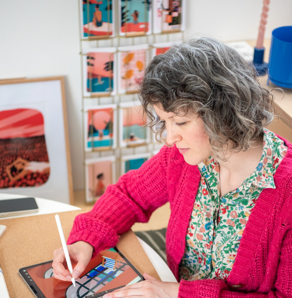 Illustratrice travaillant sur tablette graphique dans un atelier créatif avec affiches colorées en arrière-plan.