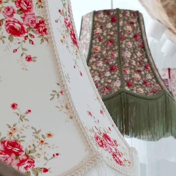 Gros plan sur deux abat-jour fleuris de style rétro, ornés de passementerie et de longues franges, l’un dans des tons clairs et l’autre dans des nuances vertes.