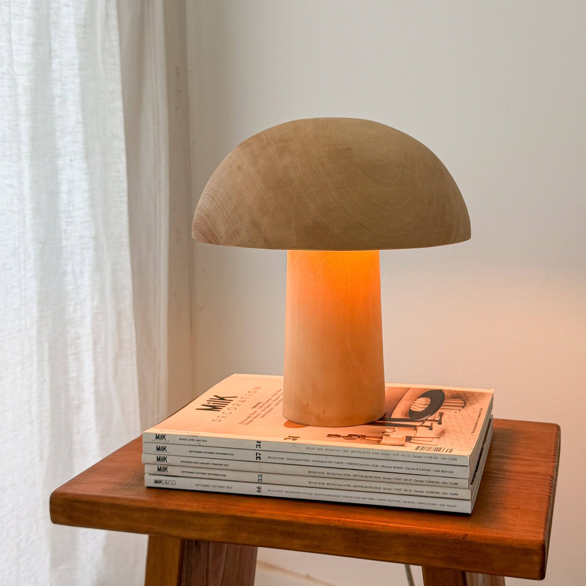 Une lampe en bois allumée, en forme de champignon posée sur des magazines.