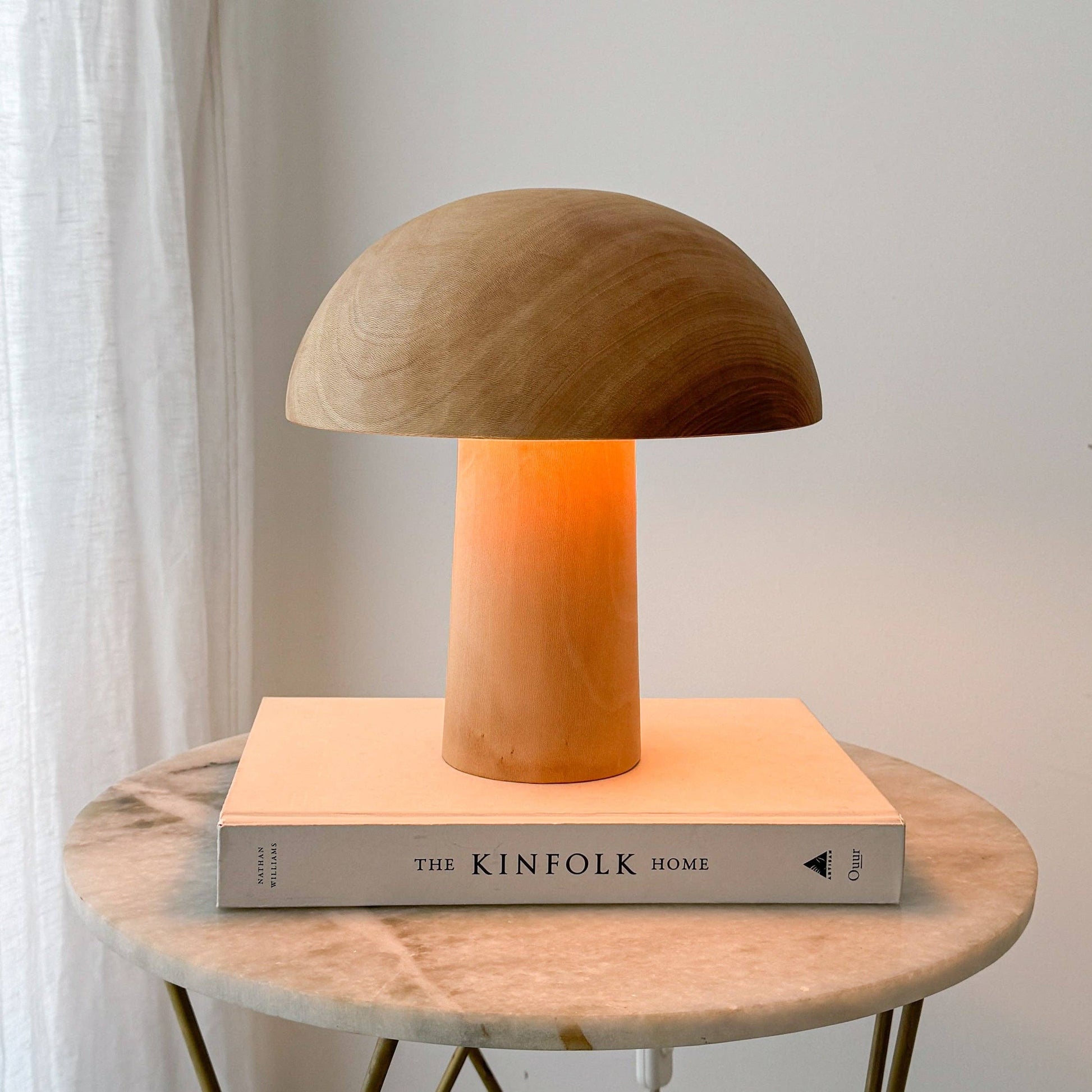 Une lampe en bois allumée, en forme de champignon posée sur un livre.