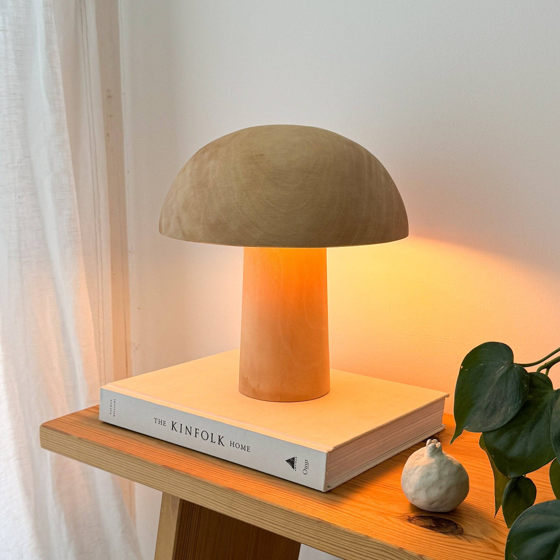 Une lampe en bois allumée, en forme de champignon posée sur un livre.