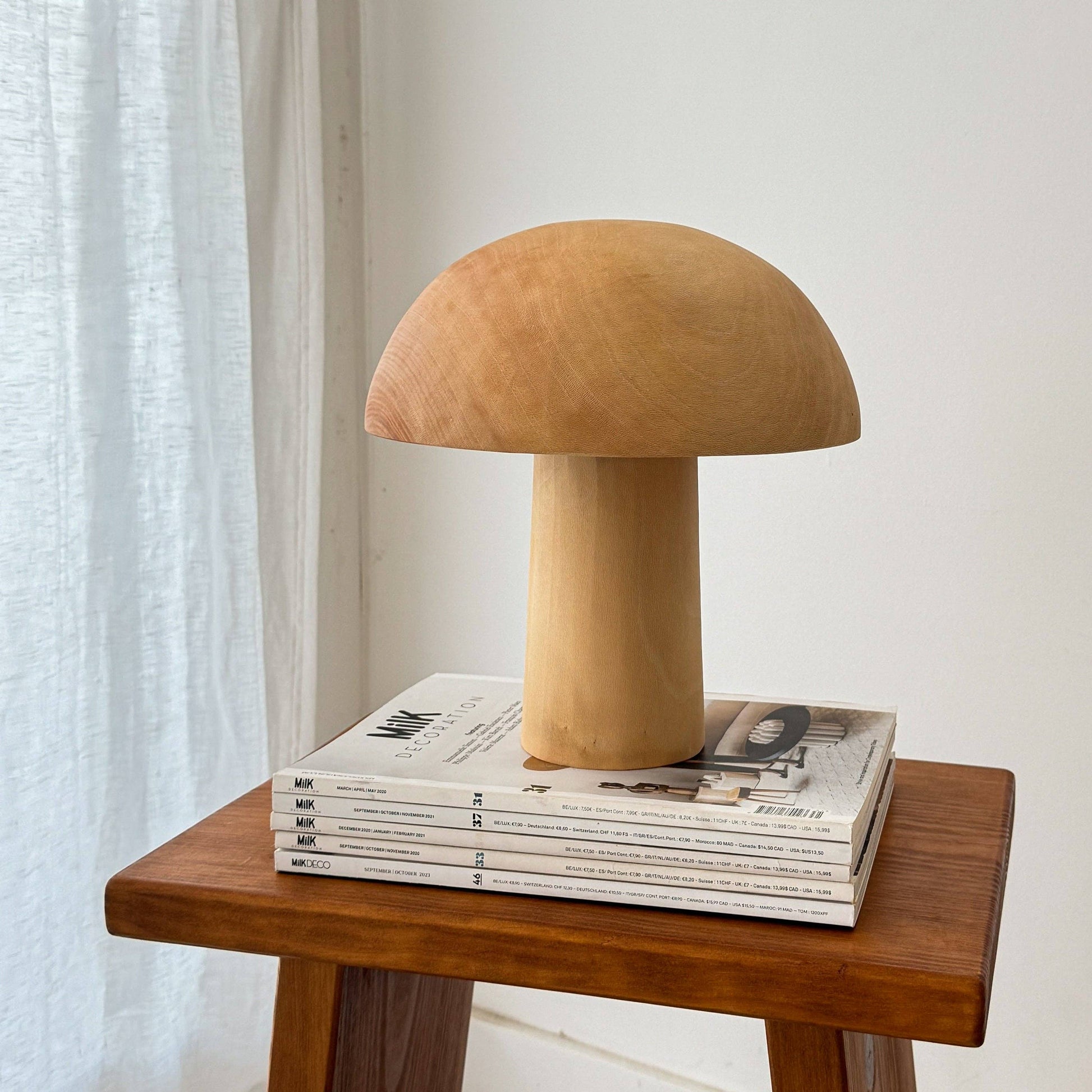 Une lampe en bois éteinte, en forme de champignon, posée sur des magazines.