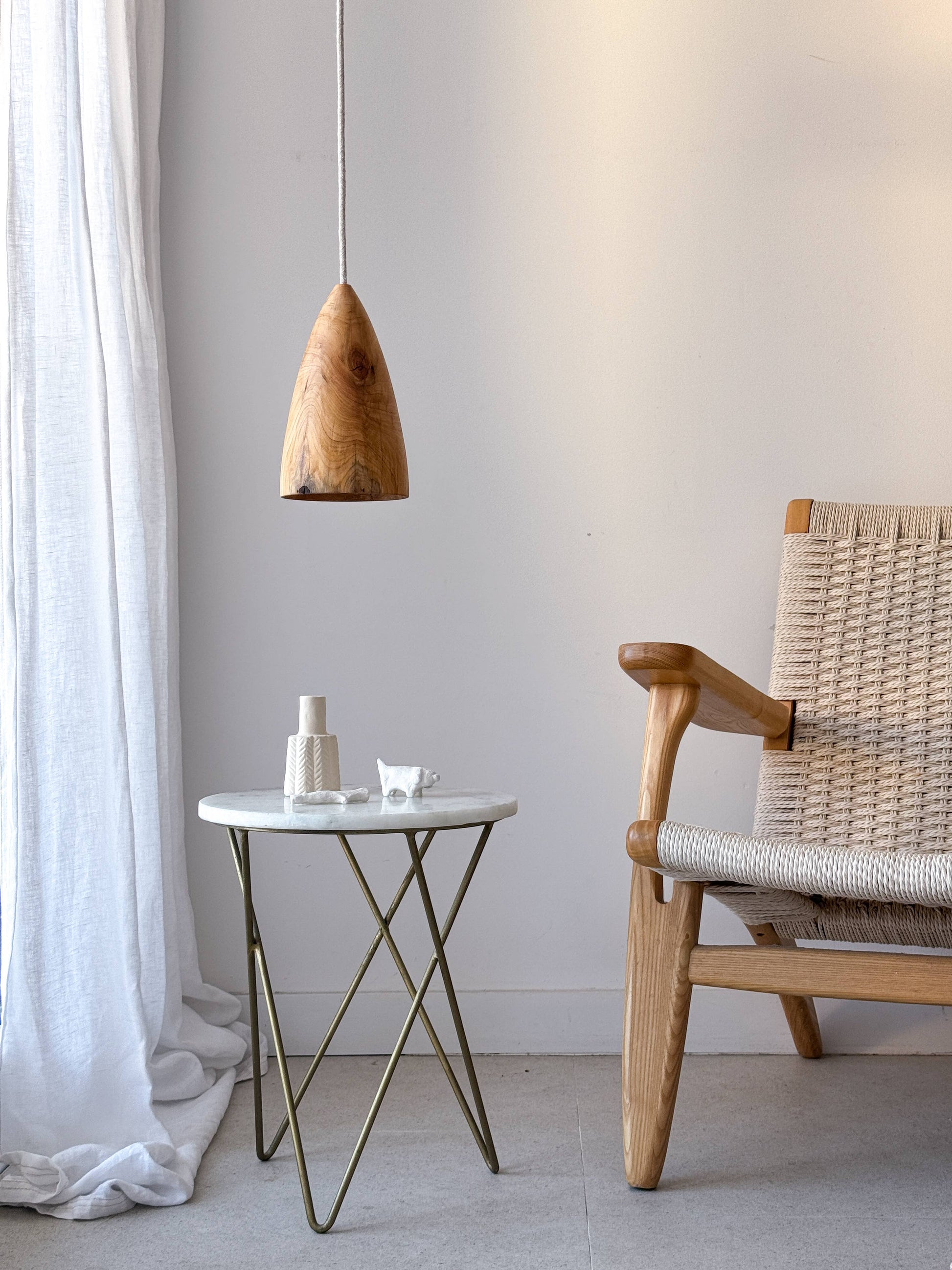 Fauteuil et table d'appoint devant une fenêtre avec un rideau blanc. Une lampe est suspendue au dessus de la table d'appoint.