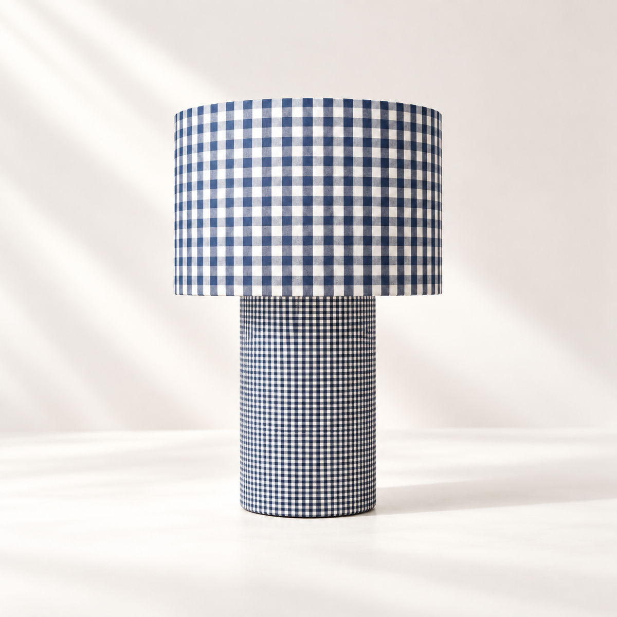 Lampe à poser habillée de deux motifs vichy bleu et blanc, avec de grands carreaux sur l’abat-jour et un motif plus fin sur le pied cylindrique.