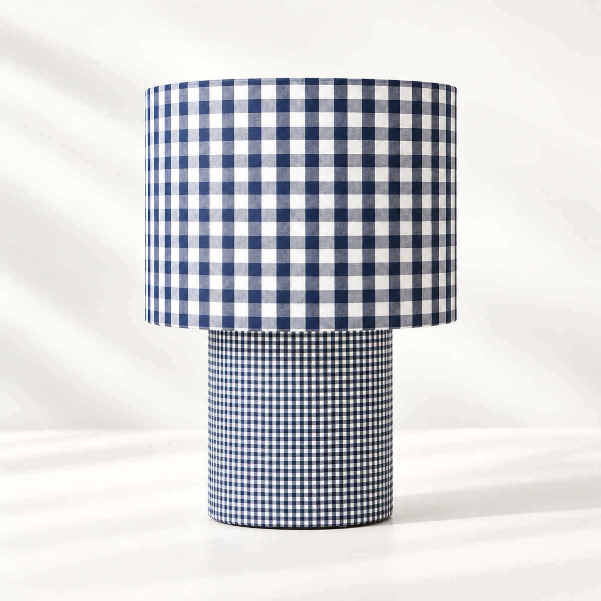 Lampe à poser habillée de deux motifs vichy bleu et blanc, avec de grands carreaux sur l’abat-jour et un motif plus fin sur le pied cylindrique.