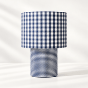 Lampe à poser habillée de deux motifs vichy bleu et blanc, avec de grands carreaux sur l’abat-jour et un motif plus fin sur le pied cylindrique.