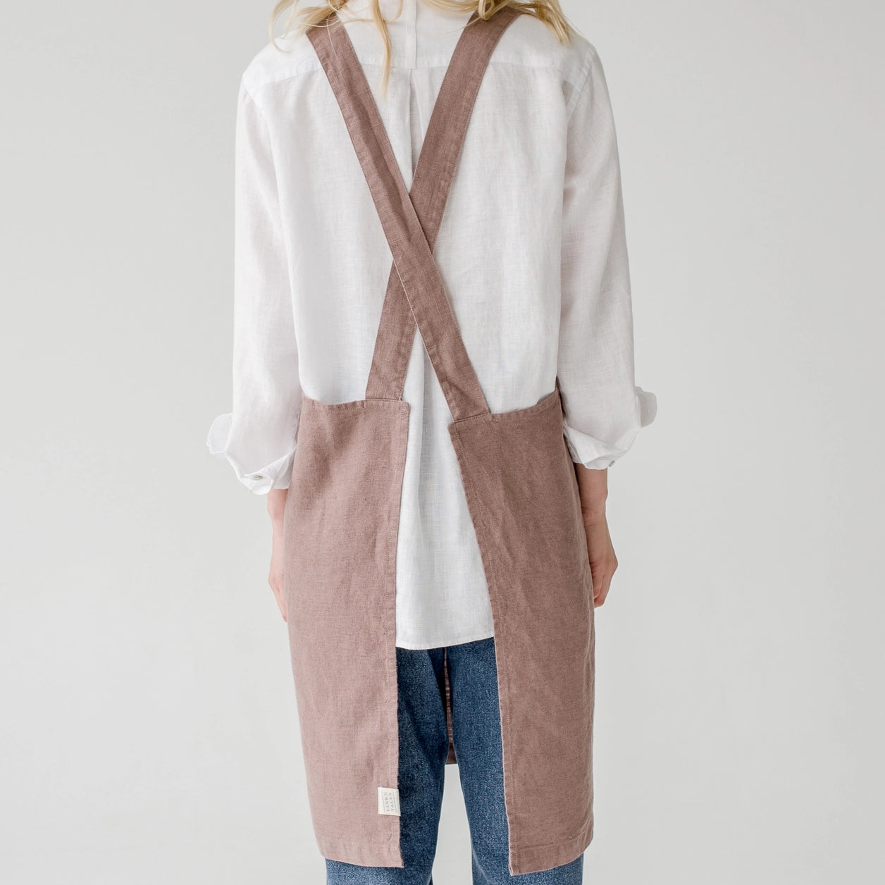 Femme de dos avec un tablier croisé de couleur bois de rose.