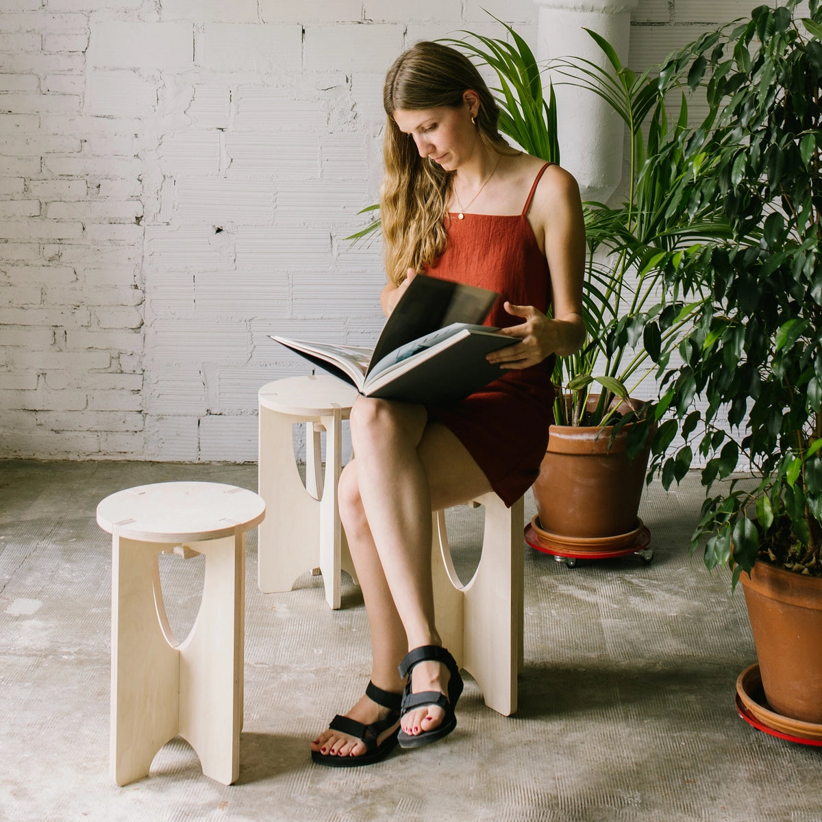 Jeune femme assise sur un tabouret en bois, entrain de lire une livre.
