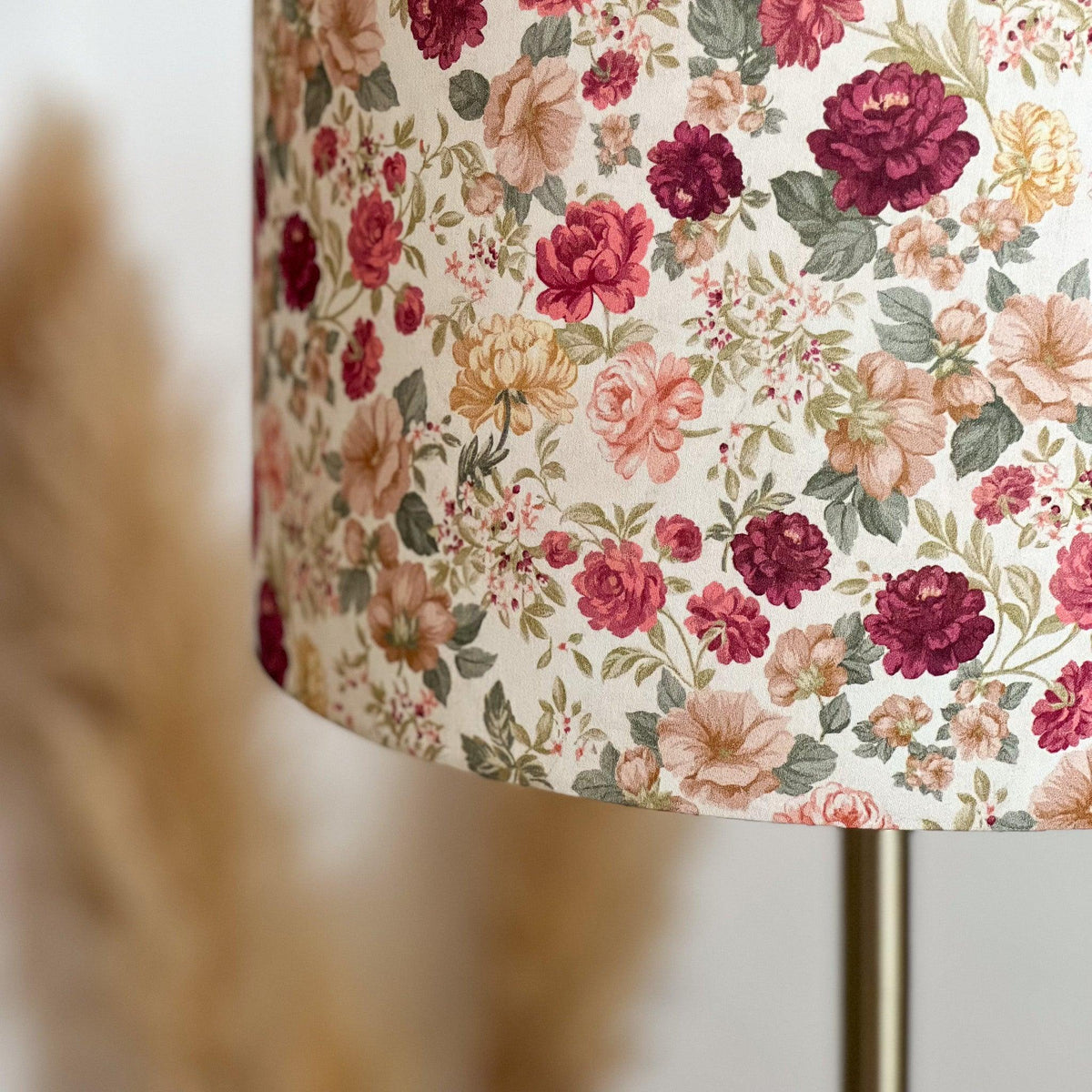 Gros plan sur un abat-jour en tissu fleuri aux tons rose, bordeaux, beige et vert, monté sur un pied de lampe en métal doré.