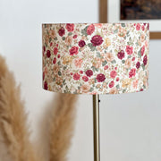 Lampadaire avec abat-jour cylindrique en tissu fleuri aux tons rose, bordeaux, beige et vert, monté sur un pied fin en métal doré.