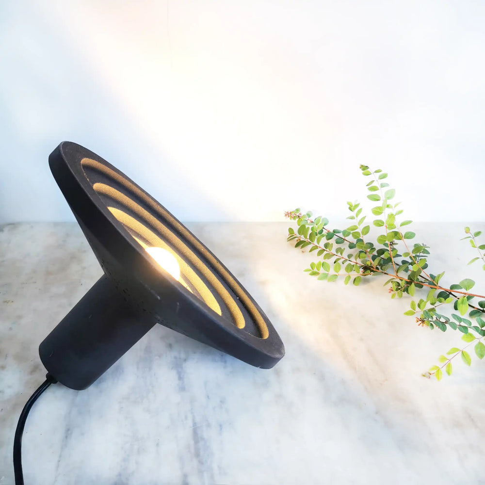 Lampe design noire avec lumière intégrée posée sur table en marbre, objet décoratif contemporain.
