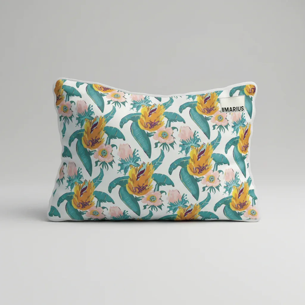 Coussin rectangulaire avec un motif floral représentant des fleurs jaunes et roses avec des feuilles vertes sur un fond blanc. Une petite étiquette avec texte est cousue dans le coin supérieur droit.